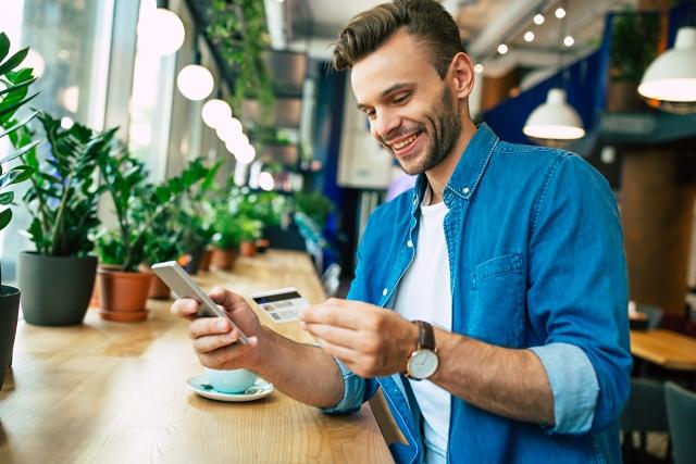 man smiling in a coffee shop as he uses a credit card