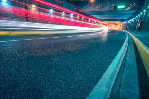 Long exposure photograph of light trails from moving vehicles through an illuminated highway tunnel