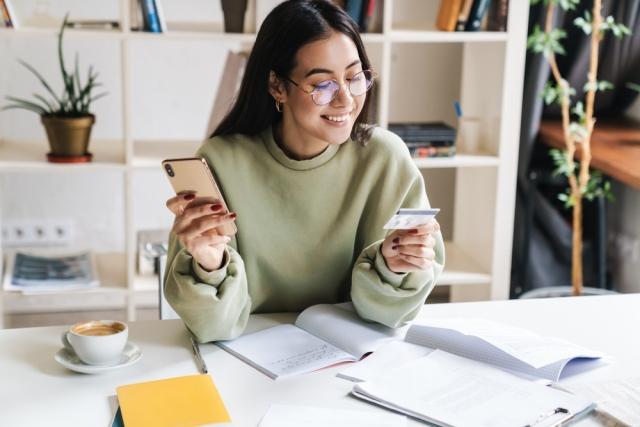 a young woman in a green sweater holding a credit card in one hand and an iphone in the other
