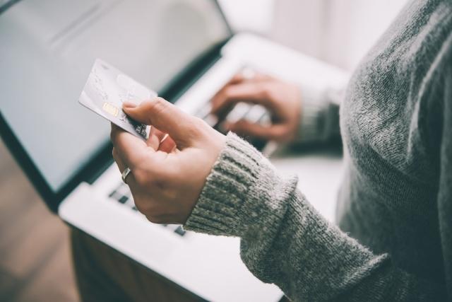 woman in gray sweater holds a credit card