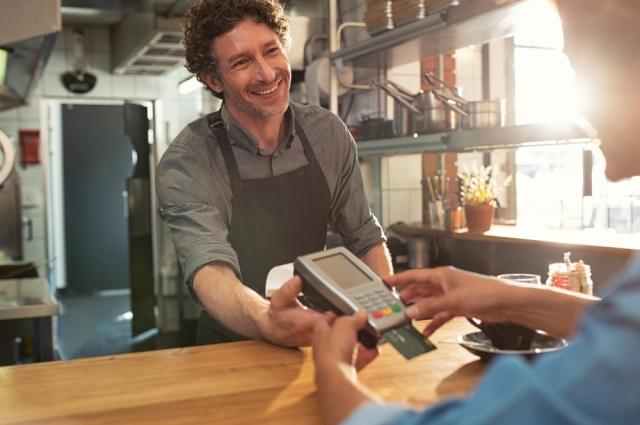 small business owner in an apron holds a card reader out 