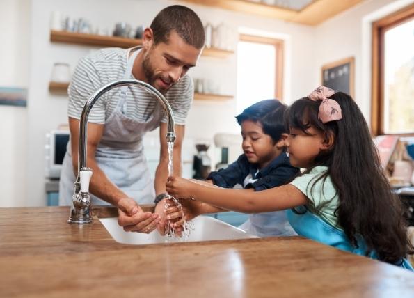a man and his children use a sink to wash their hands before preparing dinner