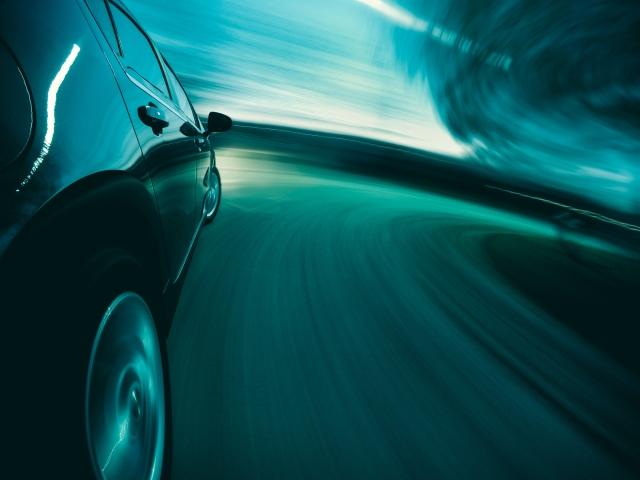 Car driving at high speed through illuminated tunnel with motion blur creating turquoise streaks