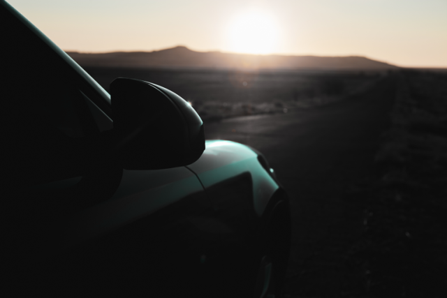 Silhouette of a car driving on a desert road at sunset with mountains in the background
