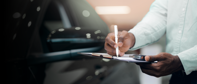 Person in light blue shirt writing on clipboard with vehicle in background