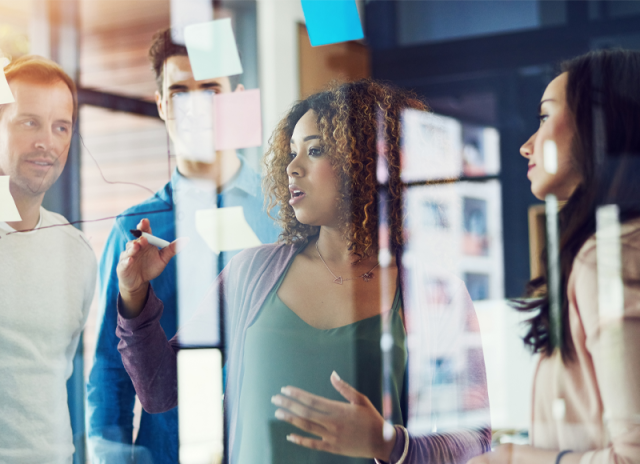 A team collaborates around a glass wall of colorful notes, representing data‑driven insight gathering and the streamlined access to JD Power analytics that supports smarter customer‑experience decisions.