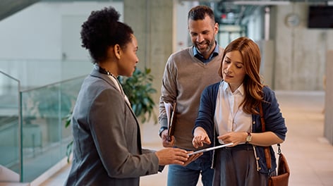 Three people, two women and one man, looking at and discussing content on a tablet in an office.