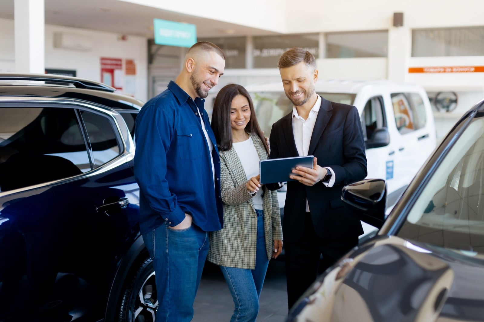 Couple with salesperson holding tablet in car showroom
