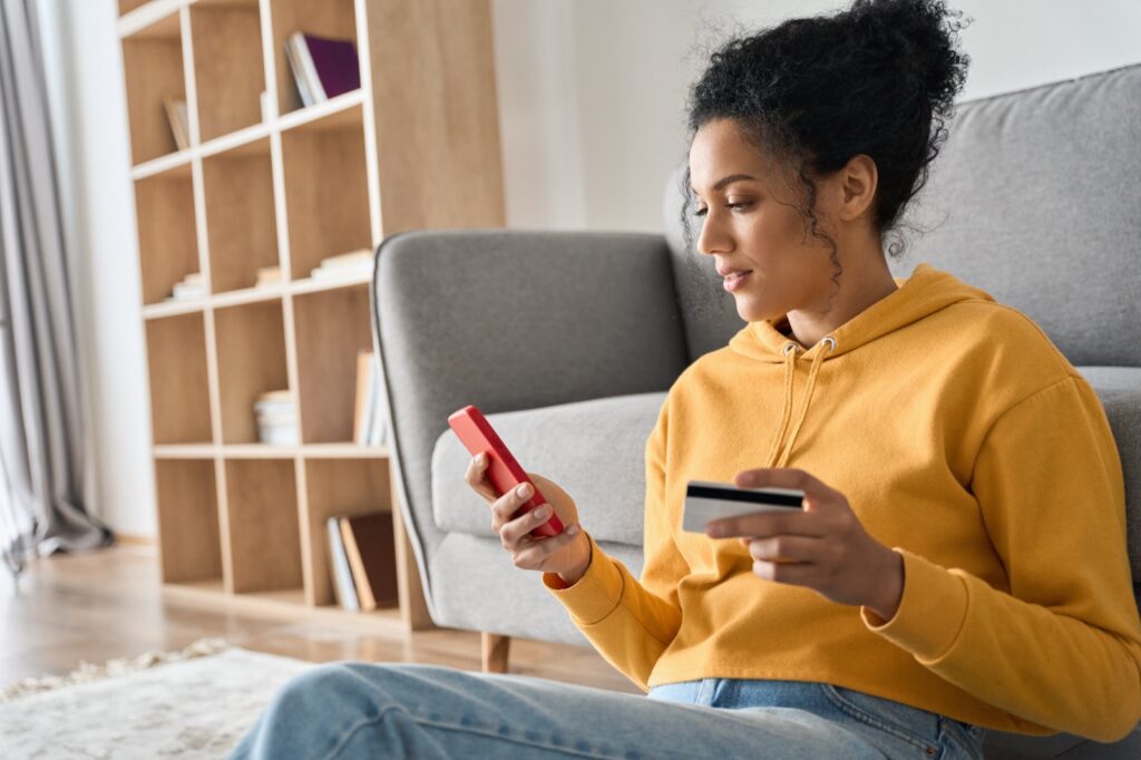 Young woman at home with smartphone & credit card shopping online