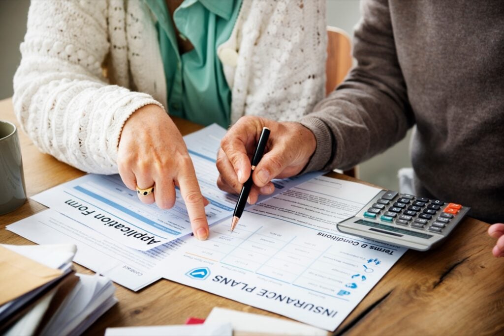 Two people at table reviewing an Insurance Plans application form with calculator