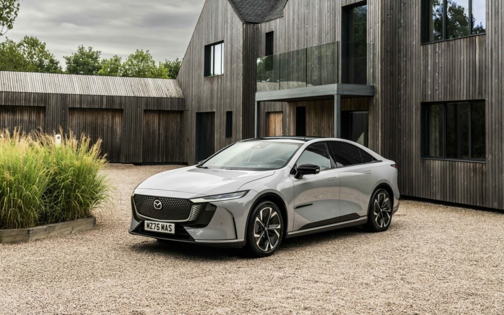 Photo of a light grey Mazda e6 in front of a house in a gravel driveway.||