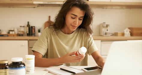Woman at home on her laptop, holding a pill bottle.