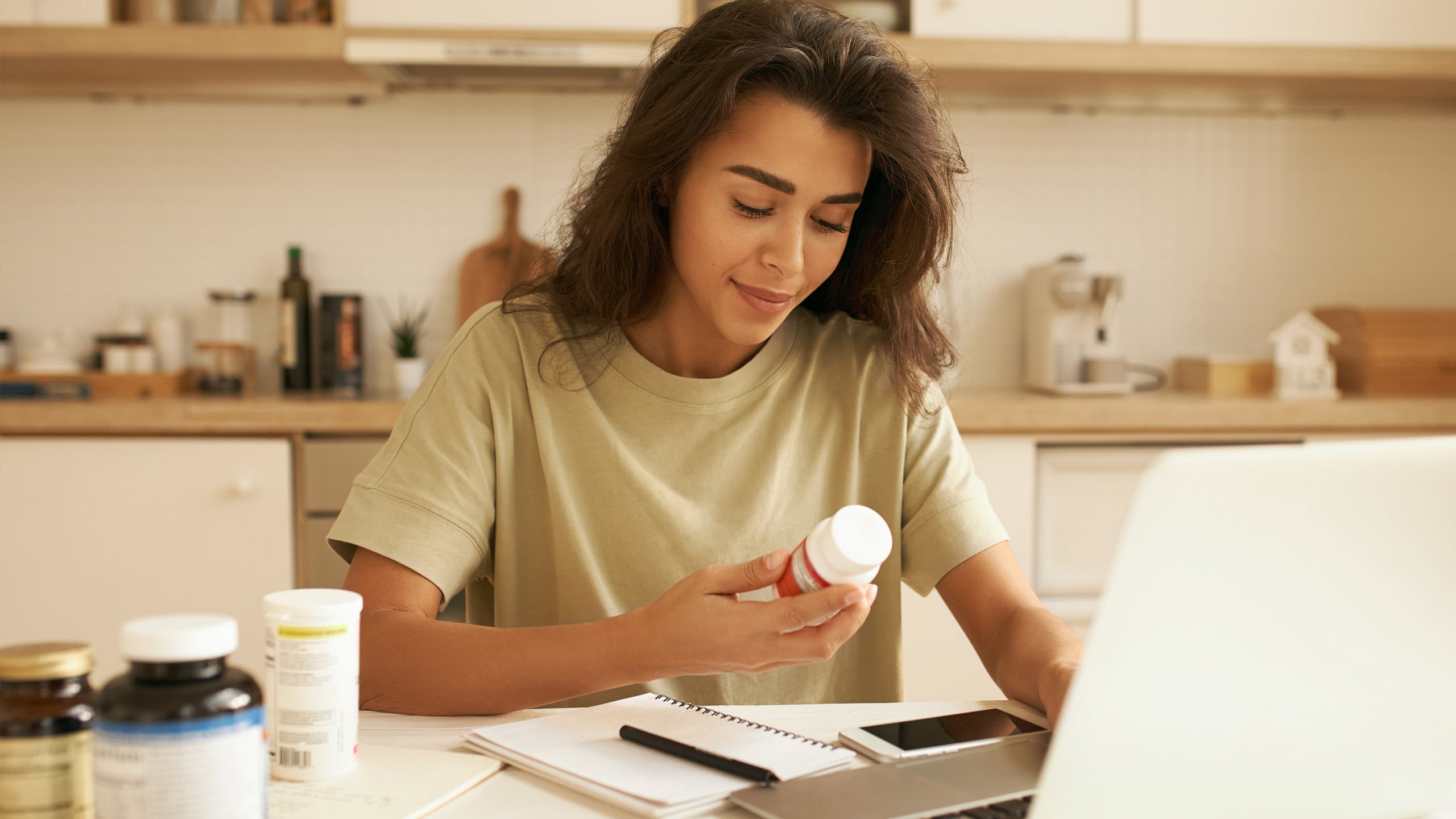 Woman at home on her laptop, holding a pill bottle.