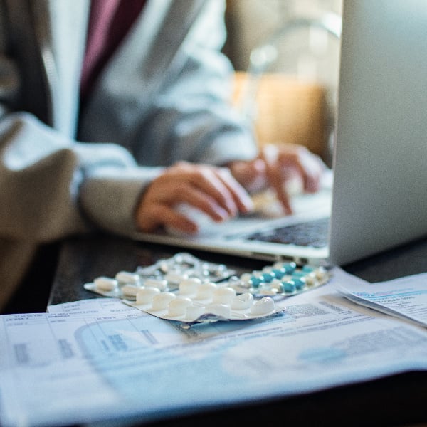 Close up of person typing on laptop at home, with a pill pack in the foreground.