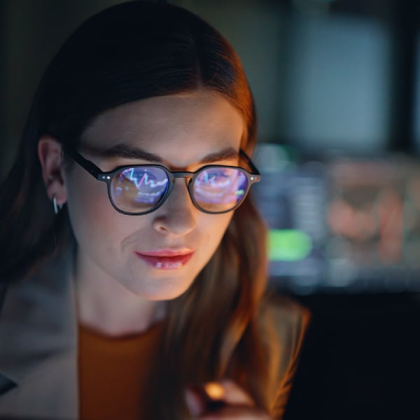 Woman looking at laptop with data graphic on screen reflecting in her glasses.