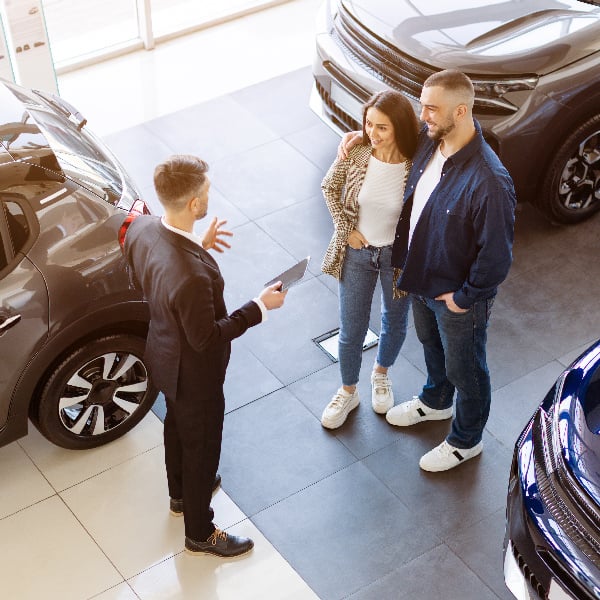 Overhead shot of salesperson talking to a couple at a car dealership.